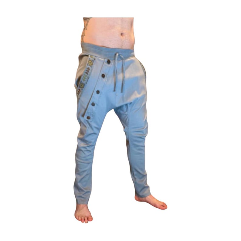Puede incluir: Pantalones har&eacute;n azul claro con bragueta abotonada y cintura con cord&oacute;n. Los pantalones presentan tela estampada decorativa a lo largo de los bolsillos laterales. Tienen un corte holgado y perneras estrechas.