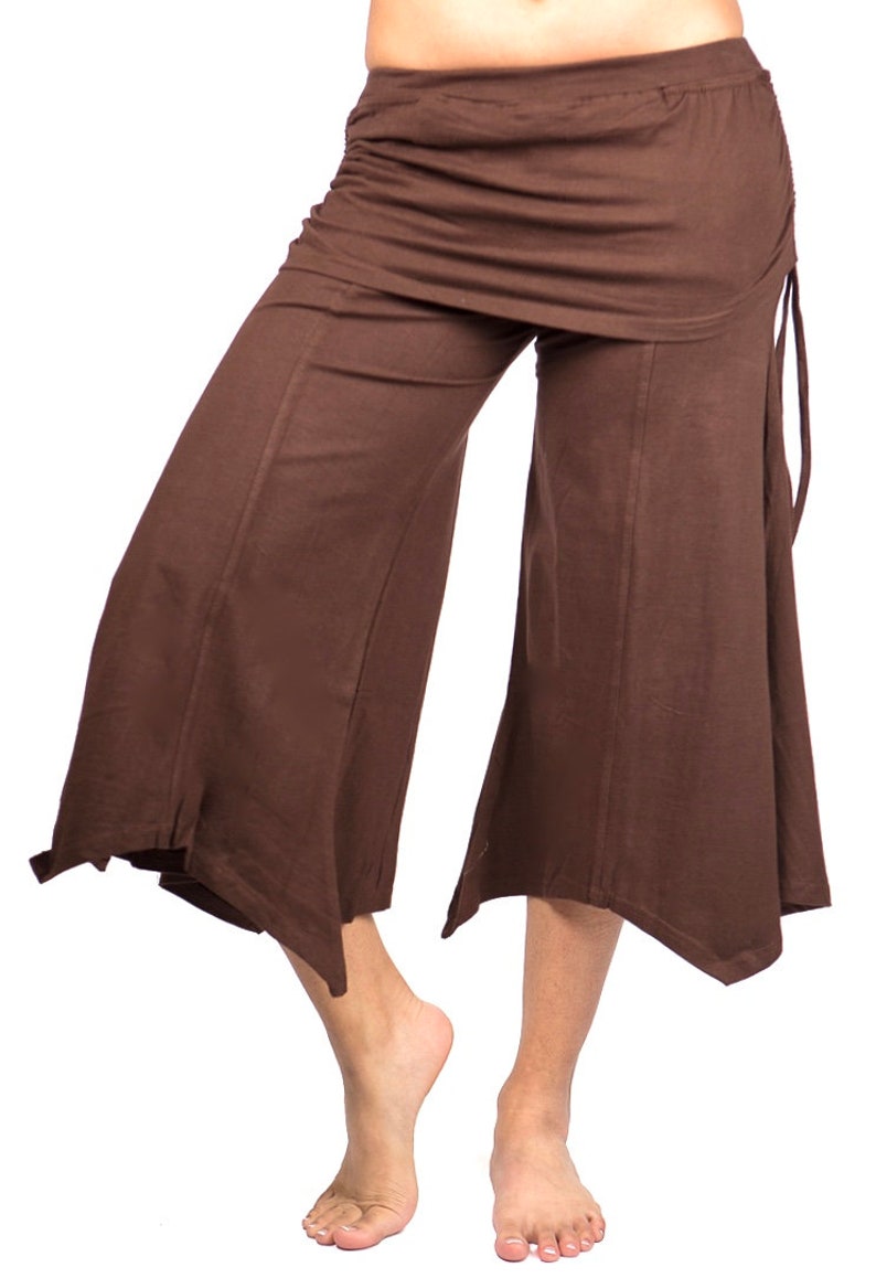 May include: Brown wide-leg pants with a draped skirt overlay and a tie at the side. The pants are made of a soft, flowing fabric.