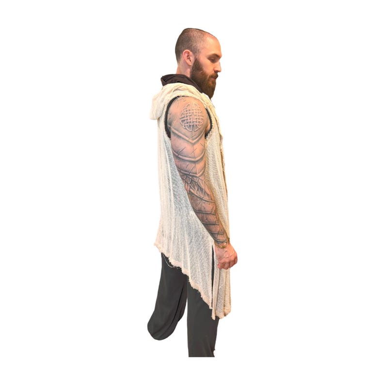 May include: A cream-colored, sleeveless hooded vest with a distressed, open-knit design. The vest has a long, asymmetrical hemline and a relaxed fit. The model is wearing dark gray pants. The vest is a unique piece of clothing.