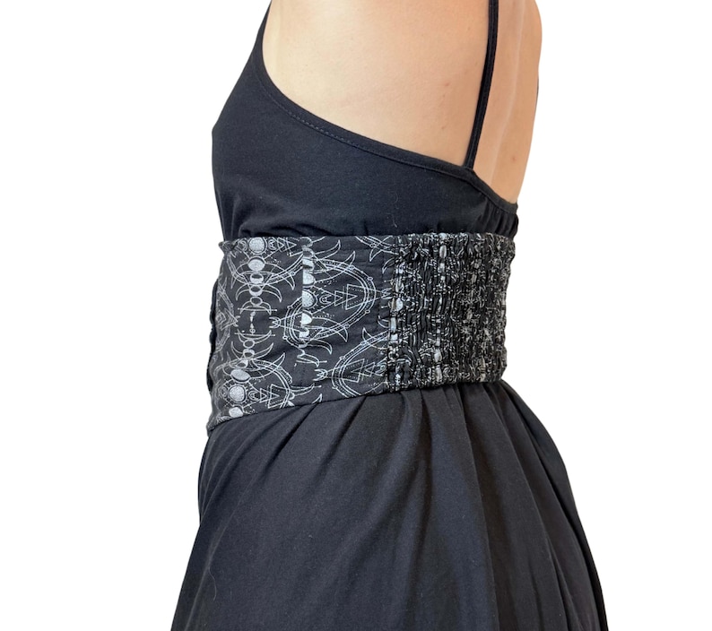 May include: Black dress with spaghetti straps and a wide, patterned belt. The belt features a repeating white design on a black background. The dress has a fitted bodice and a flowing skirt, creating a flattering silhouette.