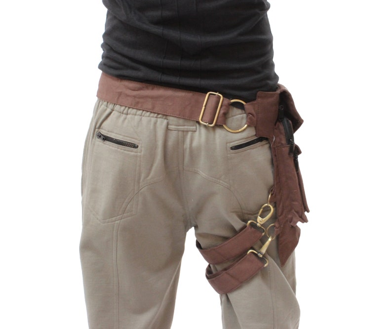 Puede incluir: Un cintur&oacute;n de cuero marr&oacute;n con una hebilla de metal y una correa de pierna de cuero marr&oacute;n con hebillas de metal. El cintur&oacute;n se lleva sobre un pantal&oacute;n beige.
