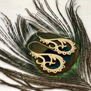 May include: A pair of gold-toned earrings with a delicate, intricate design. The earrings are shaped like a stylized flower with a curved stem. They are displayed on a peacock feather.