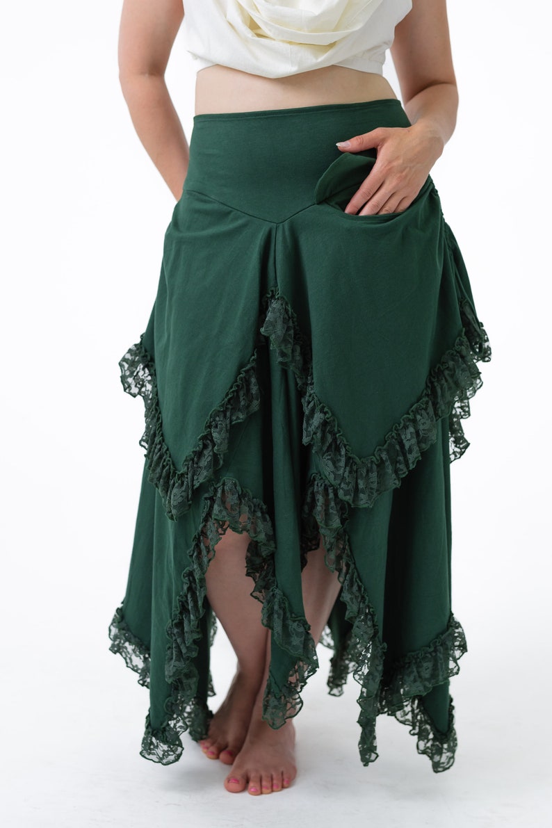 Puede incluir: Una falda verde oscuro con cintura alta y un dobladillo con volantes. La falda tiene un ribete de encaje y un bolsillo en el lateral.