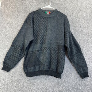 Könnte beinhalten: Ein grauer Pullover mit Patchwork-Design. Der Pullover hat verschiedene strukturierte Muster, darunter Rauten- und Rippenabschnitte. Die Manschetten und der Saum sind dunkler grau. Ein kleines Etikett mit dem Wort "Italy" ist am Kragen sichtbar.