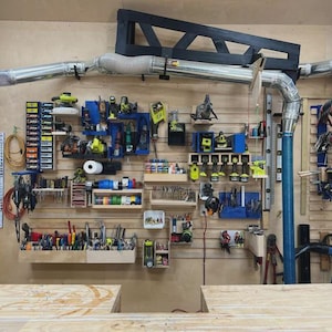May include: A workshop wall with various tools and equipment organized on shelves and racks. Power tools, hand tools, and accessories are neatly arranged. Electrical cords and hoses are also visible, along with a dust collection system.