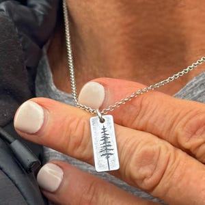 May include: A silver chain necklace with a rectangular pendant featuring a detailed etched tree design.