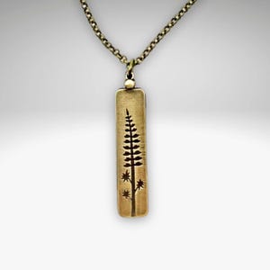 May include: A gold necklace with a pendant featuring a stylized tree design. The pendant is rectangular and has a textured surface.