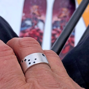 May include: A silver ring with a design of black diamonds on the band.