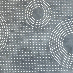 May include: A gray textile with a pattern of white dotted circles. The circles vary in size and are arranged across the fabric. The background is a solid gray color. The textile has a Japanese character in the lower right corner.