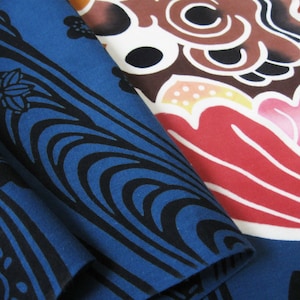 May include: A close-up of blue fabric with a black wave pattern. The fabric is folded over itself, revealing a red and pink floral pattern on the underside.