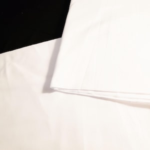 以下が含まれることがあります： 黒い表面に折り畳まれた白い綿の枕カバー2枚