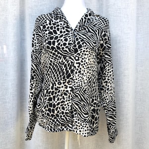 May include: A black and white long-sleeved button-up shirt with a mixed animal print pattern. The shirt has a collared neckline and a button closure.