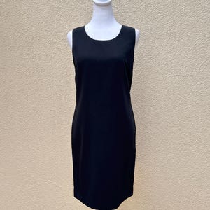 May include: A sleeveless black dress with a round neckline. The dress is fitted and falls to the knee.