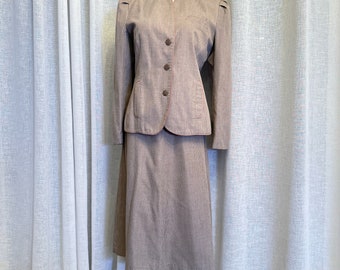 May include: A brown and gray skirt suit with a pink trim. The jacket has a mandarin collar and four buttons. The skirt is knee-length.