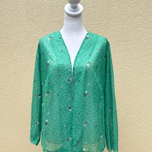 May include: A green sheer blouse with a floral print. The blouse has a V-neck and long sleeves.