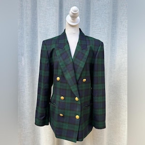 May include: A double-breasted blazer in a green and navy plaid pattern. The jacket features gold-colored buttons and a classic notched lapel. The blazer is displayed on a mannequin.