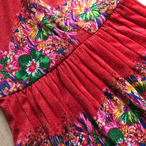 May include: Red dress with a floral print. The dress has a V-neckline and a gathered skirt.