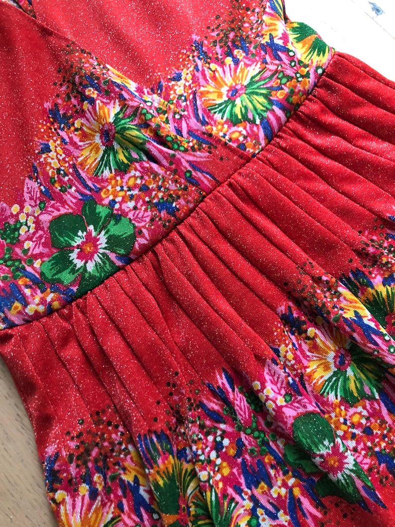 May include: Red dress with a floral print. The dress has a V-neckline and a gathered skirt.