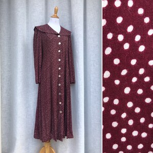 May include: A long-sleeved, burgundy dress with a white polka dot pattern and a white button-up front. The dress has a large, white collar.