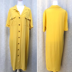 May include: A bright yellow button-down dress with short sleeves and a collared neckline. The dress features two chest pockets and a row of buttons down the front. The dress is displayed on a mannequin.