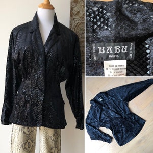 May include: Black velvet blazer with a snakeskin pattern. The blazer has a collar, long sleeves, and two pockets. The label reads "BABU PARIS" and "MODELE DEPOSE".