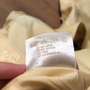 May include: A white care label with black text that reads "Do not wash, Do not bleach, Hot iron, Dry cleanable (P)". The label has several symbols including a triangle with an X inside, a circle with an X inside, an iron with two dots, and a circle with a P inside.