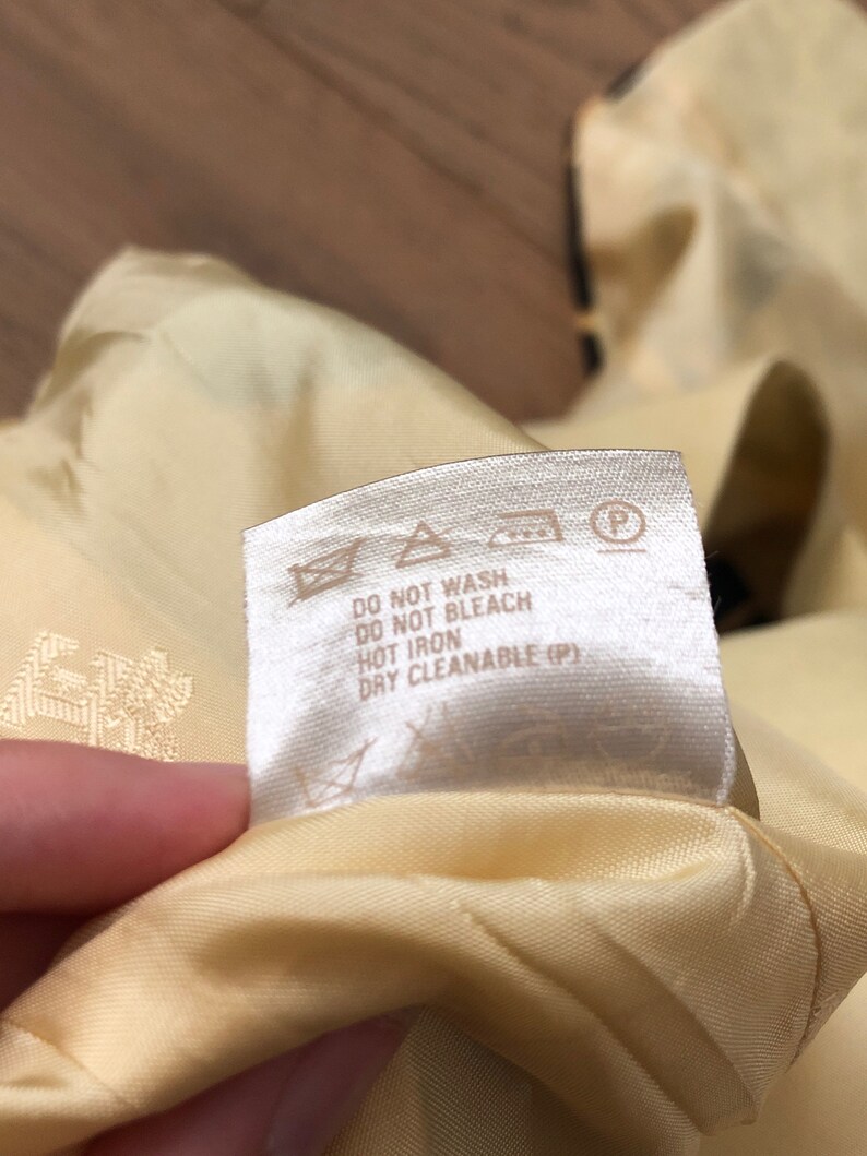 May include: A white care label with black text that reads "Do not wash, Do not bleach, Hot iron, Dry cleanable (P)". The label has several symbols including a triangle with an X inside, a circle with an X inside, an iron with two dots, and a circle with a P inside.