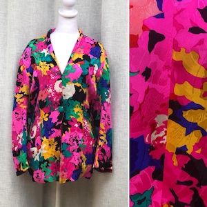 May include: A vibrant, floral-print blazer in shades of pink, yellow, green, blue, and black. The jacket features a V-neck, long sleeves, and a single button closure. The fabric has a silky sheen.