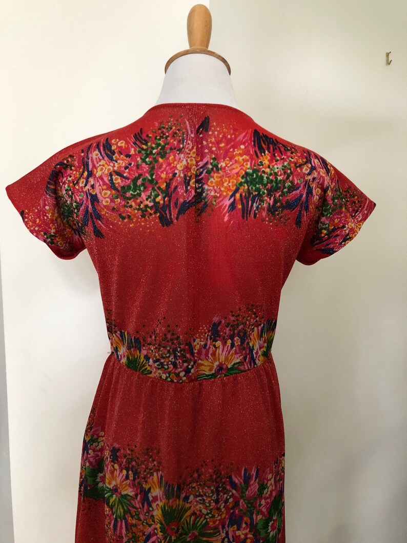 May include: A red dress with a floral print. The dress has a V-neckline and short sleeves. The fabric is a sparkly, textured material.