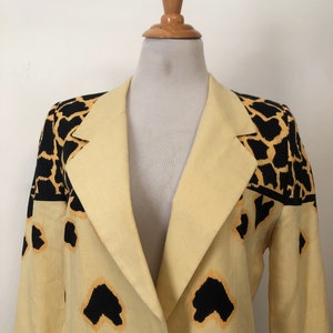 May include: A yellow blazer with a black and orange animal print design. The blazer has a long sleeve and a collar.