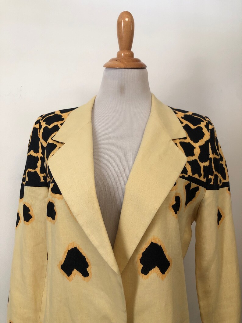 May include: A yellow blazer with a black and orange animal print design. The blazer has a long sleeve and a collar.
