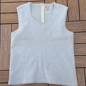 May include: A light blue sleeveless sweater with a scoop neck and a cream-colored zipper. The sweater has a ribbed hem and a tag with text. The garment is made of a soft, knitted material.