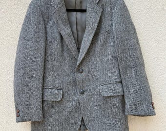 May include: A gray herringbone tweed blazer with two button closures. The blazer has a classic fit and features a single chest pocket and two front pockets.