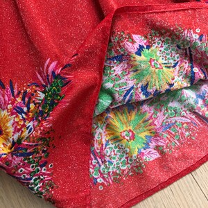May include: Red fabric with a glittery texture and a floral print in shades of pink, green, yellow, and blue.