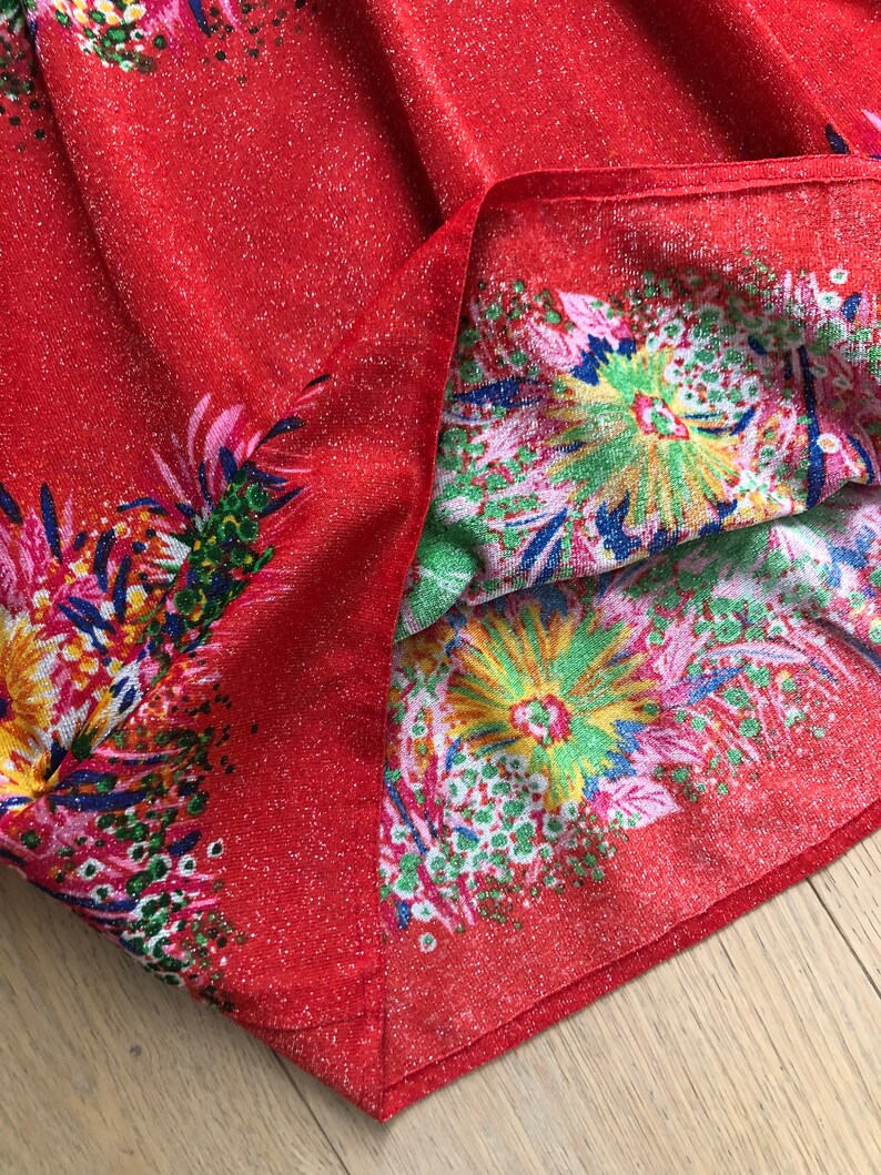 May include: Red fabric with a glittery texture and a floral print in shades of pink, green, yellow, and blue.