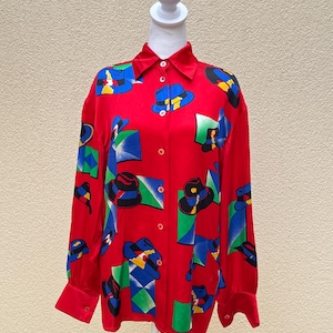 May include: A red long-sleeved button-up shirt with a colorful geometric pattern featuring hats. The shirt has a collared neckline and long sleeves with button cuffs.