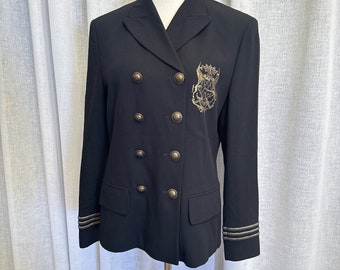 May include: A black double-breasted blazer with gold accents and a gold embroidered crest on the right side. The blazer has a classic collar and long sleeves with gold trim.
