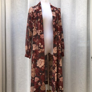 K&ouml;nnte beinhalten: Eine lange, maronfarbene, durchsichtige Robe mit Blumendruck. Die Robe hat einen Schalkragen und einen Bindeg&uuml;rtel.