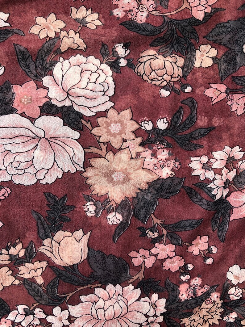 K&ouml;nnte beinhalten: Ein burgunderfarbener Stoff mit einem floralen Muster aus rosa, wei&szlig;en und beigefarbenen Blumen. Die Blumen sind in einem sich wiederholenden Muster angeordnet und haben eine Vintage-&Auml;sthetik.