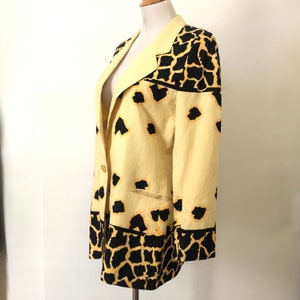 May include: A yellow blazer with a black and yellow animal print. The blazer has a single button closure and a pocket on the left side.