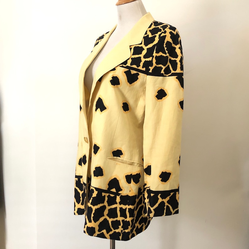 May include: A yellow blazer with a black and yellow animal print. The blazer has a single button closure and a pocket on the left side.