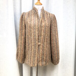 May include: A vintage tweed jacket in shades of brown, beige, and red, displayed on a mannequin. The jacket features a high collar, long sleeves, and a single button closure. The fabric has a textured, woven appearance.