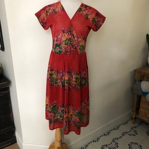 May include: A red midi dress with a floral print. The dress has a V-neckline and short sleeves. It is made of a lightweight fabric and has a flowy silhouette.