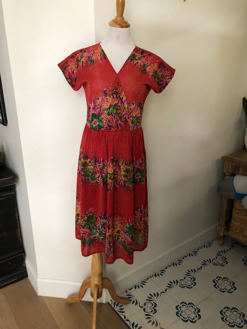 May include: A red midi dress with a floral print. The dress has a V-neckline and short sleeves. It is made of a lightweight fabric and has a flowy silhouette.