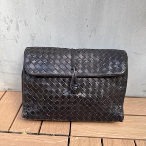 May include: A black leather woven clutch bag with a knotted closure.