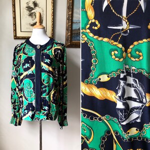 May include: A navy blue and green silk blouse with a nautical print featuring anchors, chains, and ships. The blouse has a button-up front and long sleeves.