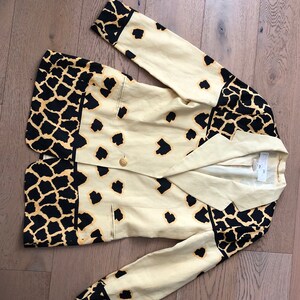 May include: A beige blazer with a black and yellow animal print. The blazer has a double breasted closure and a pocket on the left side.