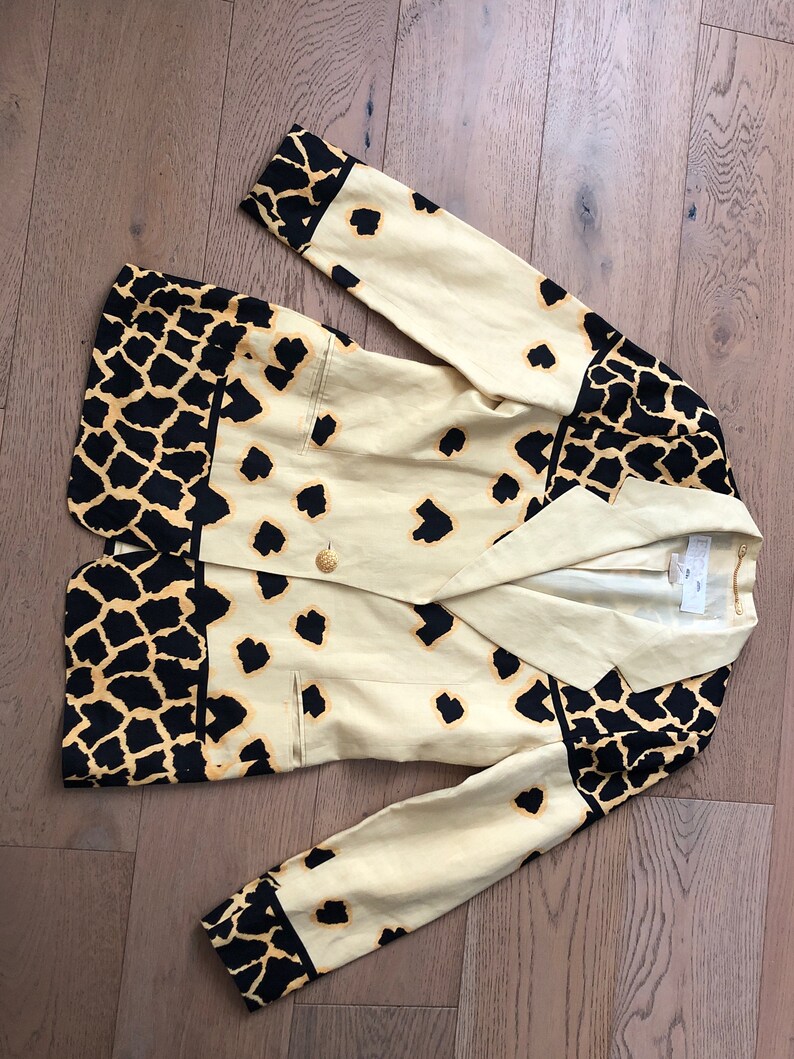 May include: A beige blazer with a black and yellow animal print. The blazer has a double breasted closure and a pocket on the left side.