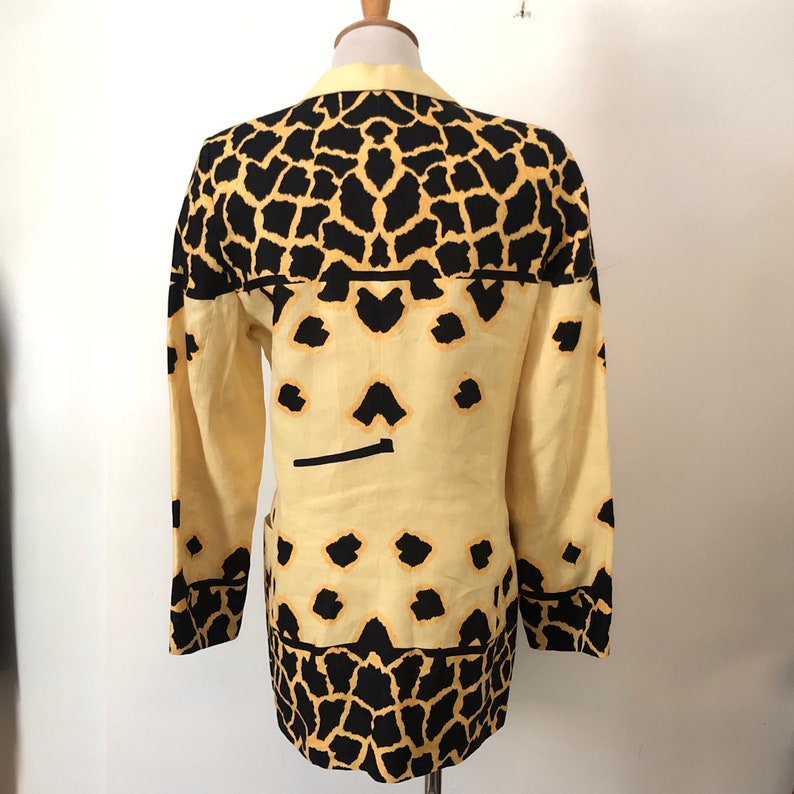 May include: A yellow and black patterned blazer with a giraffe print. The blazer has a long sleeve and a button closure.