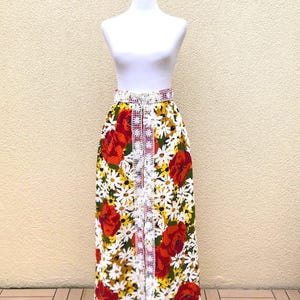 May include: A long white skirt with a floral print featuring red poppies and yellow daisies. The skirt has a white lace trim down the front and a red waistband.